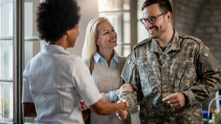 Veterano de uniforme estrechando la mano a una mujer mientras otra mujer mira sonriendo.